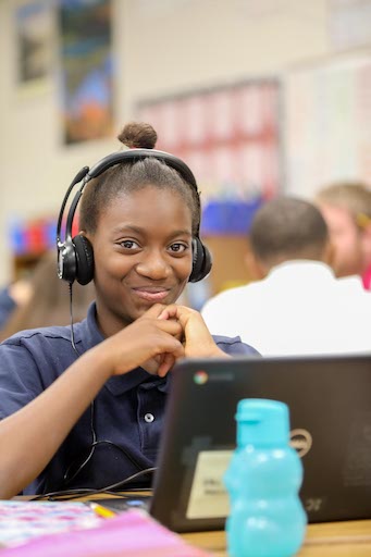 Student posing in class wearing headphones and using a laptop